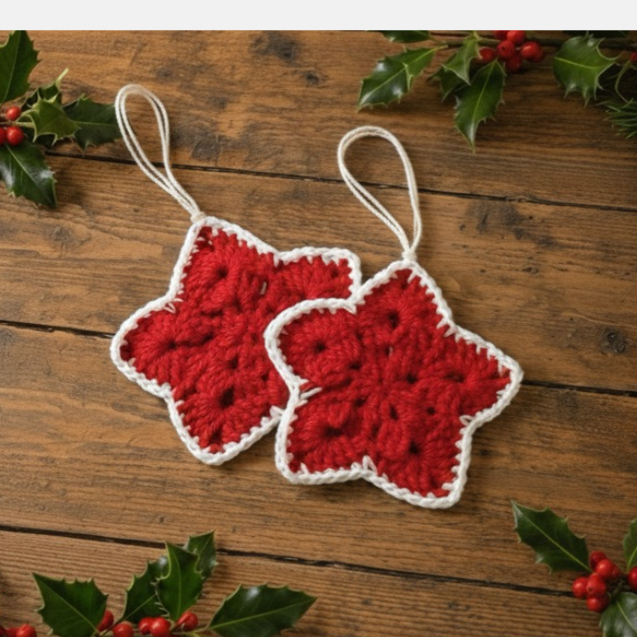 Two red crocheted star ornament on a wooden surface with holly leaves and berries.