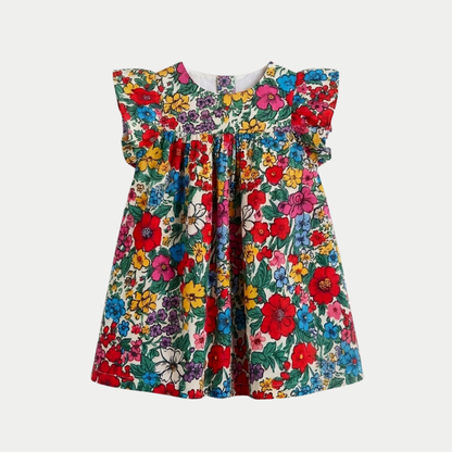 A toddler girl's dress featuring a vibrant, dense floral print with red, yellow, blue, and purple flowers on a cream background, complete with ruffled cap sleeves.