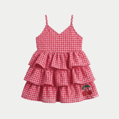 A red and white gingham tiered baby dress with spaghetti straps and a cherry embroidery on the hem, shown against a light gray background.